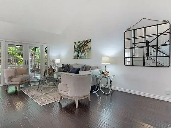 Living room with light sofa, round glass coffee table, wall mirror, and glass doors to patio.