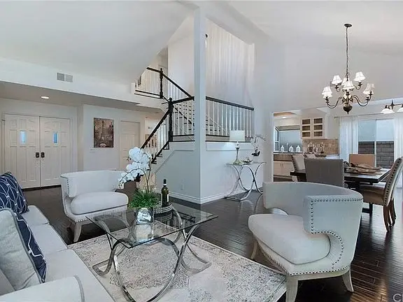 Living room with white sofa, pillows, glass coffee table, stairs, and view to dining and kitchen.