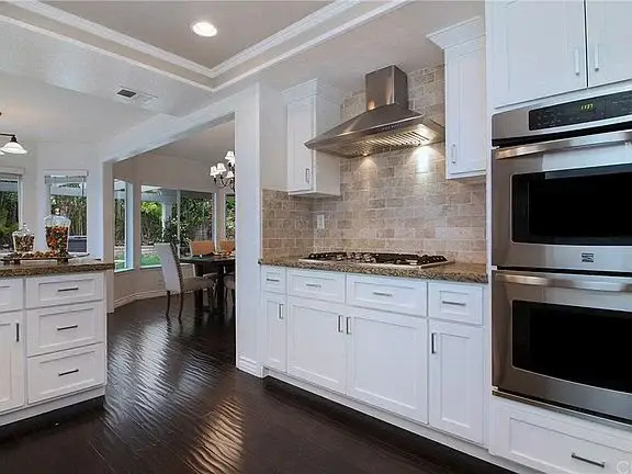 Kitchen with white cabinets, stone backsplash, stainless appliances, and wood floor.