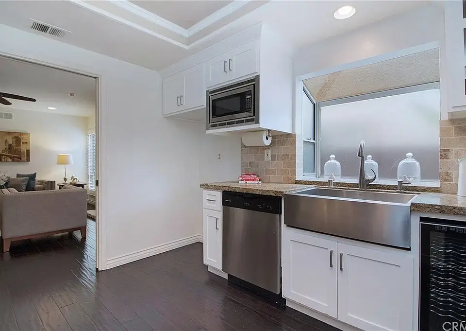 Kitchen with white cabinets, stainless sink, microwave, granite counter, and view to living room.