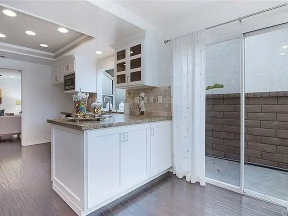 Kitchen with white cabinets, granite counter, sliding glass door to patio, lights, and candy jar.