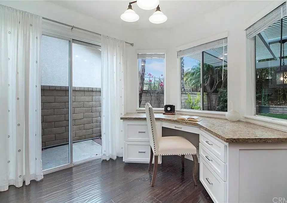 Home office with granite desk, chair, big windows, curtains, and book on desk.