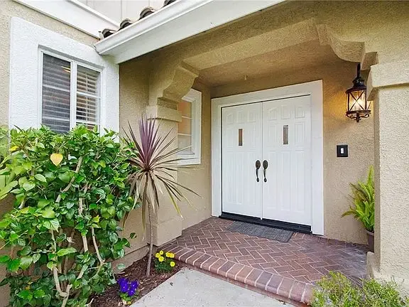 Front entrance of house California real estate with double white doors, plants, and brick pathway.