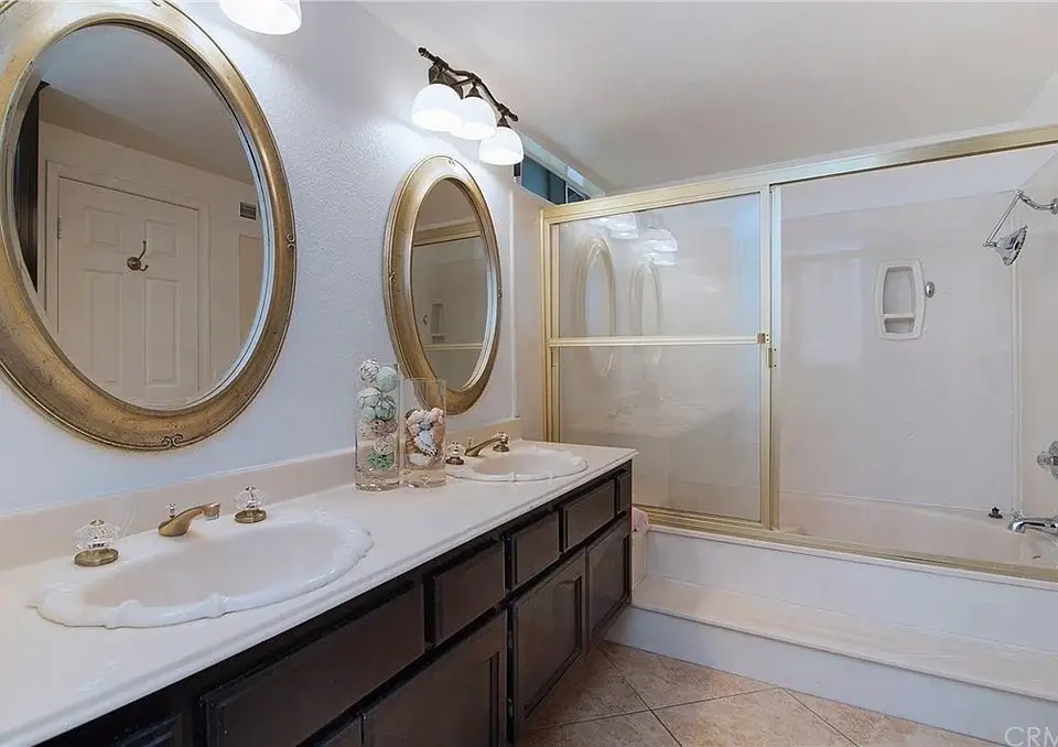 Bathroom with double sink vanity, two round mirrors, glass shower, bathtub, and tile floor.