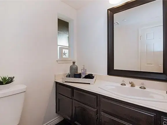 Bathroom with dark wood cabinet, white counter, large mirror, toilet, and small plant.