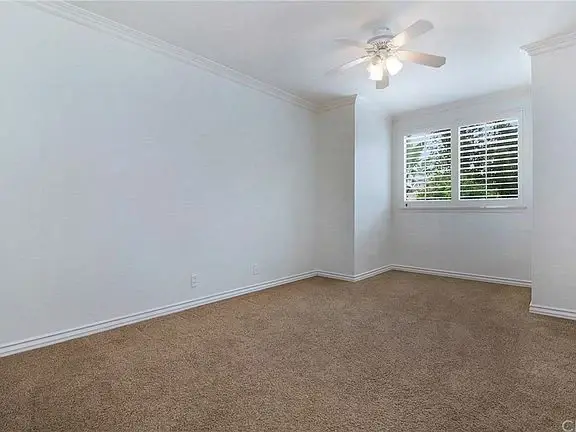 Empty room with ceiling fan, beige carpet, white walls, and window