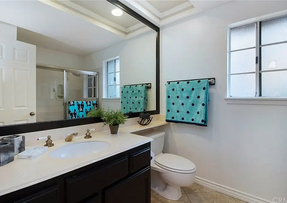 Bathroom with large mirror, sink with dark cabinets, toilet, and colorful towels.