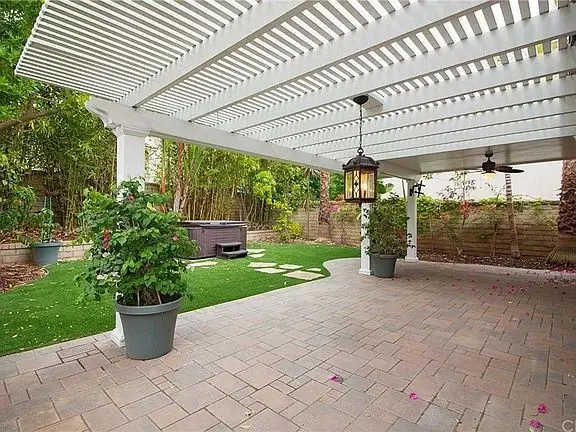 Covered patio of house California real estate with pergola, hot tub, plants, and greenery.