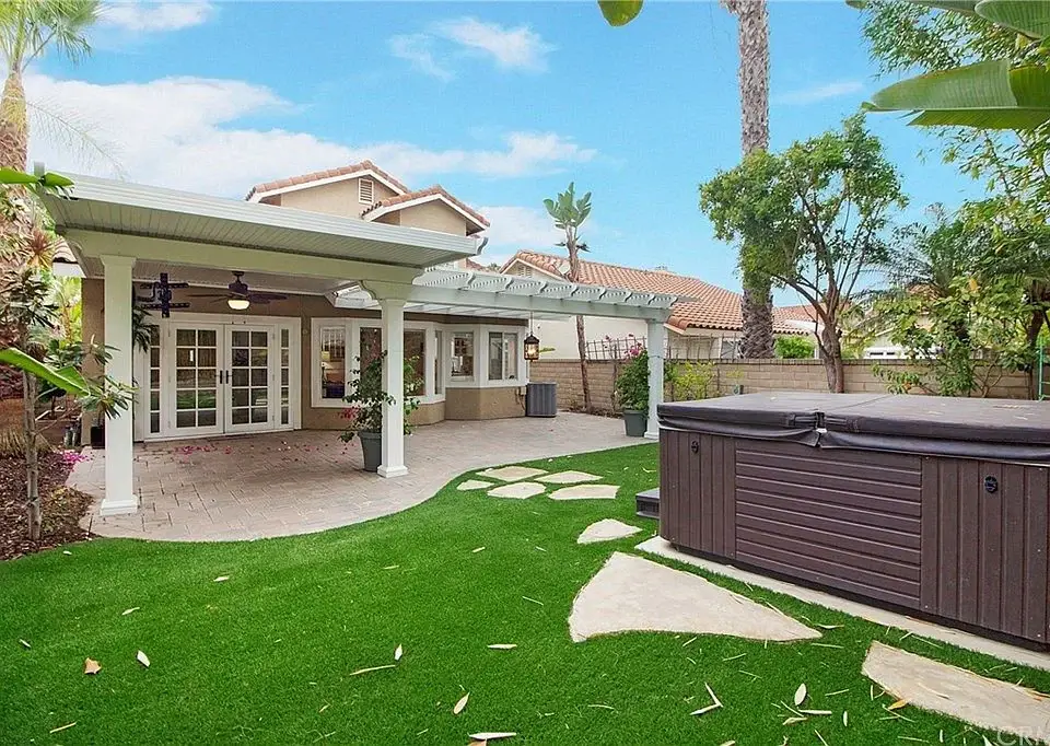 Backyard of house California real estate with patio pergola, hot tub, and green plants.