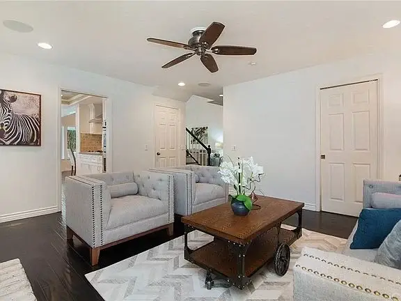 Living room with tufted armchairs, wood coffee table, rug, ceiling fan, wall art, and open doorway.
