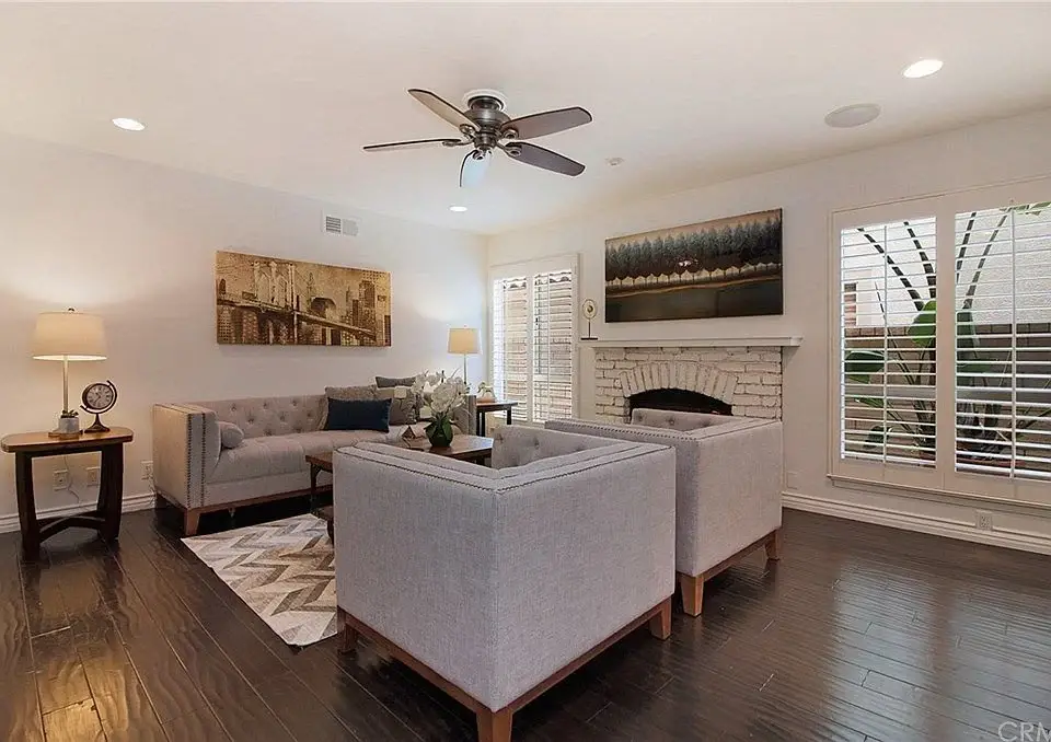 Living room with two gray sofas, coffee table, rug, ceiling fan, windows with shutters, and wall art.