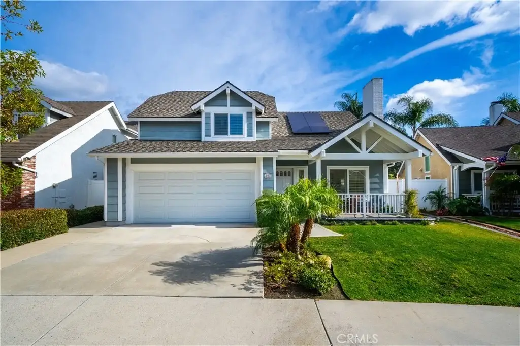 Two story house California real estate with blue exterior, front porch, solar panels, and palm trees.