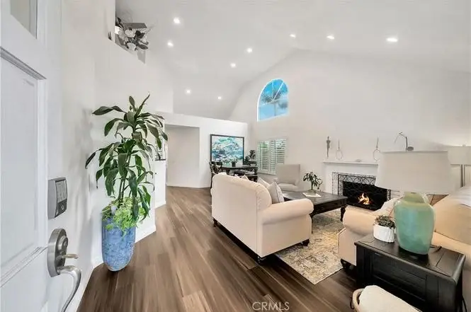 Living room with white sofa, fireplace, big windows, plant, and seating area.