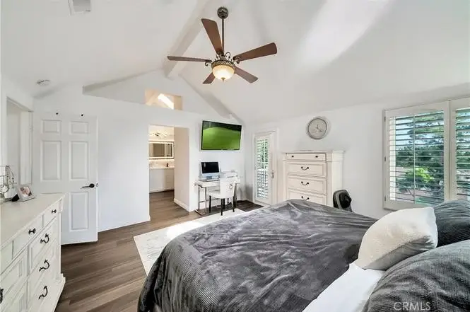 Bedroom with large bed, ceiling fan, windows with shutters, dresser, desk with computer, and wood floor.