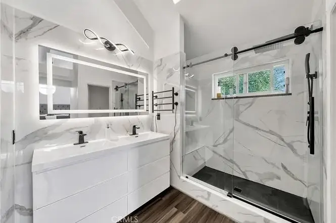Bathroom with double sink vanity, large mirror, marble walls, and glass walk in shower.
