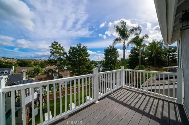 Balcony view of yard with trees and houses California real estate under blue sky with clouds.