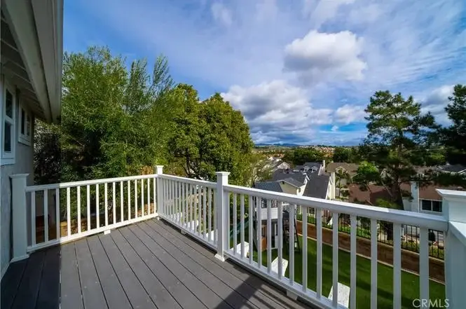 Deck with white railings overlooking houses, trees, and cloudy sky California real estate.