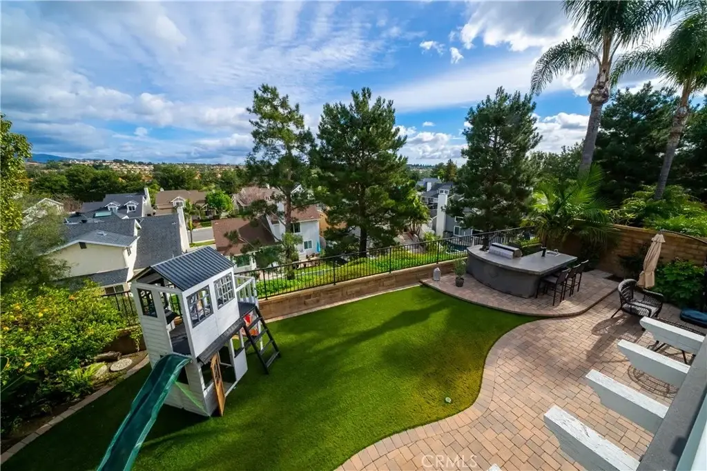 Backyard of house California real estate with playhouse, green slide, patio bar with stools, and trees.