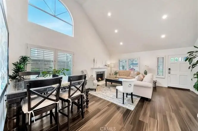 Living area with sofa seating, dining table with chairs, big windows, and wood floor.