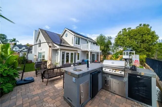 Outdoor kitchen of house California real estate with grill, dining area, plants, and home in back.
