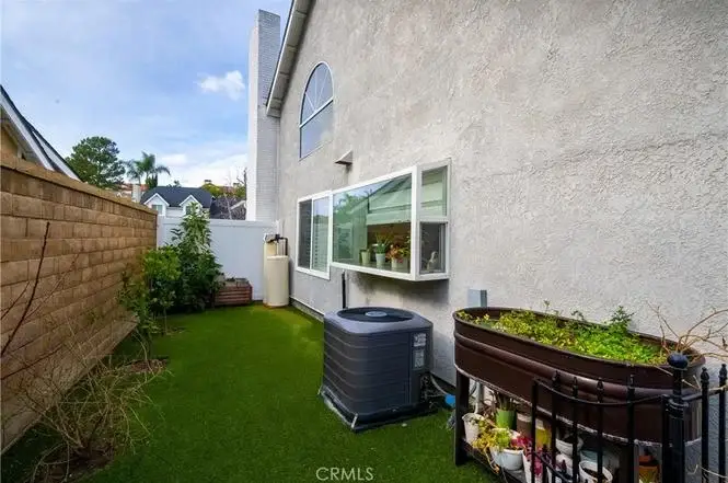 Backyard of house California real estate with green grass, AC unit, planters, fence, and window.