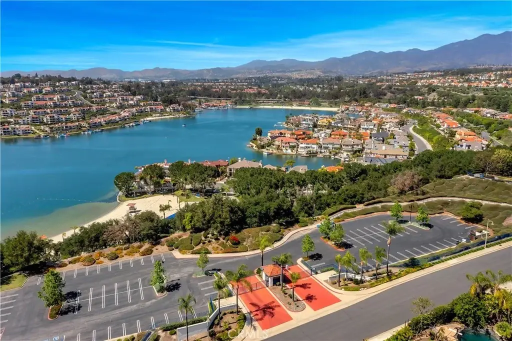 Aerial view of lake with houses California real estate, mountains, palm trees, parking area, and walkway.