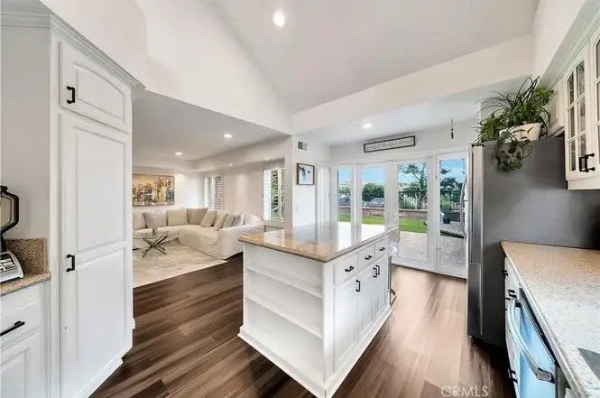 Kitchen with white cabinets, island, hardwood floor, big windows, sliding doors, and living room in back.