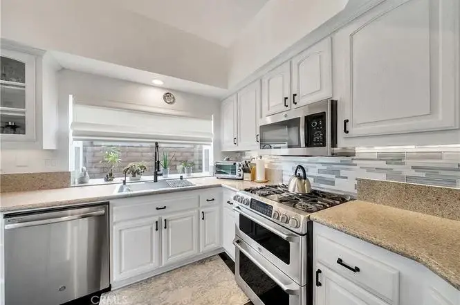 Kitchen with white cabinets, gas stove, microwave, stainless appliances, granite counter, and sink window.