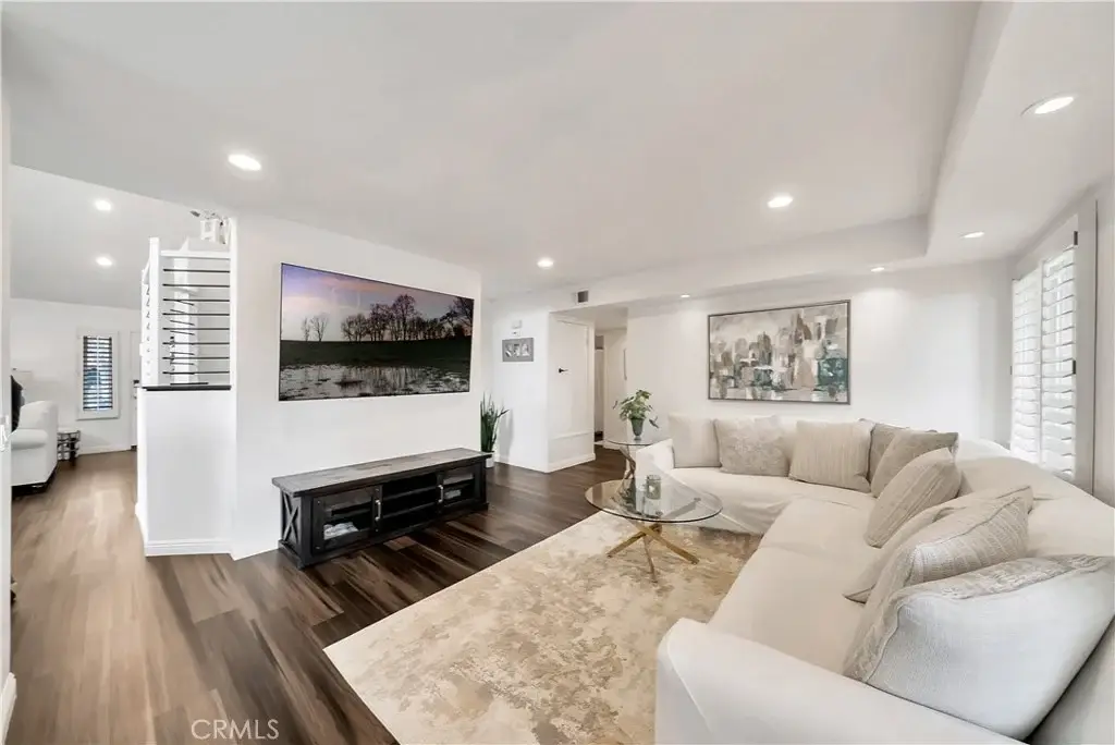 Living room with light sofa, coffee table, wall TV, decor items, wood floor, and beige rug.