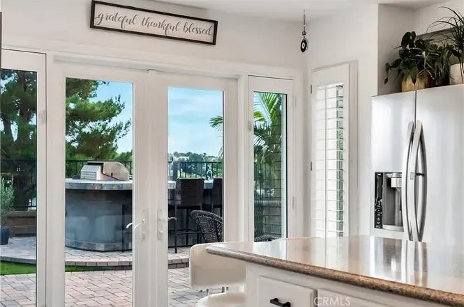 Kitchen with white cabinets, counter, big glass doors to patio, plants outside, and wall sign.