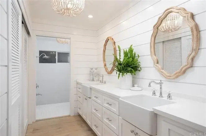 Bathroom with double sink vanity, round mirrors, white shiplap walls, plants, and shower entrance.