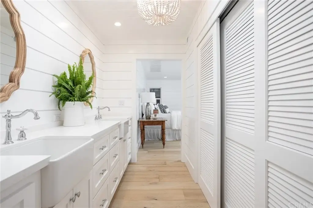 Bathroom corridor with double sinks, mirrors, white shiplap walls, plant, and wood floor.