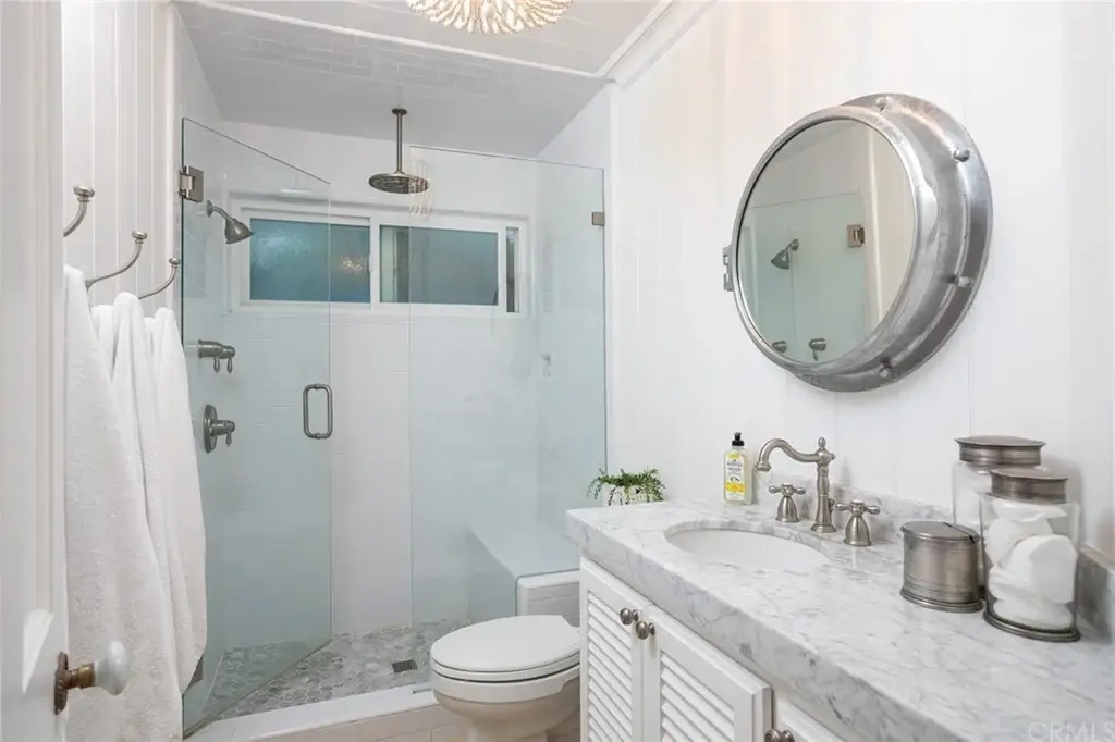 Bathroom with glass shower, round mirror, sink with silver faucet, white cabinets, towel, and marble counter.