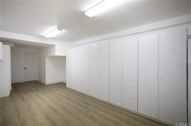 Room with white walls, built in cabinets, wood floor, and door.