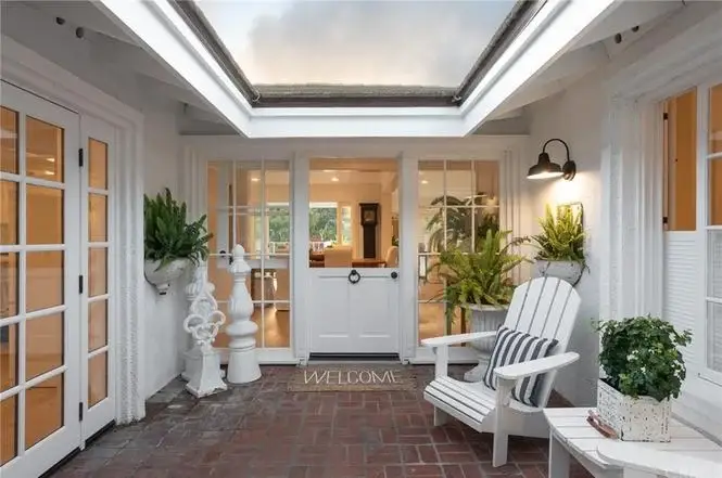 House California real estate front door with welcome mat, potted plants, rocking chair, and brick path.