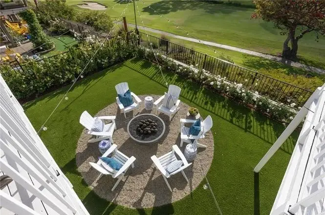 Aerial view of California real estate house backyard with fire pit, white chairs, grass, and string lights.