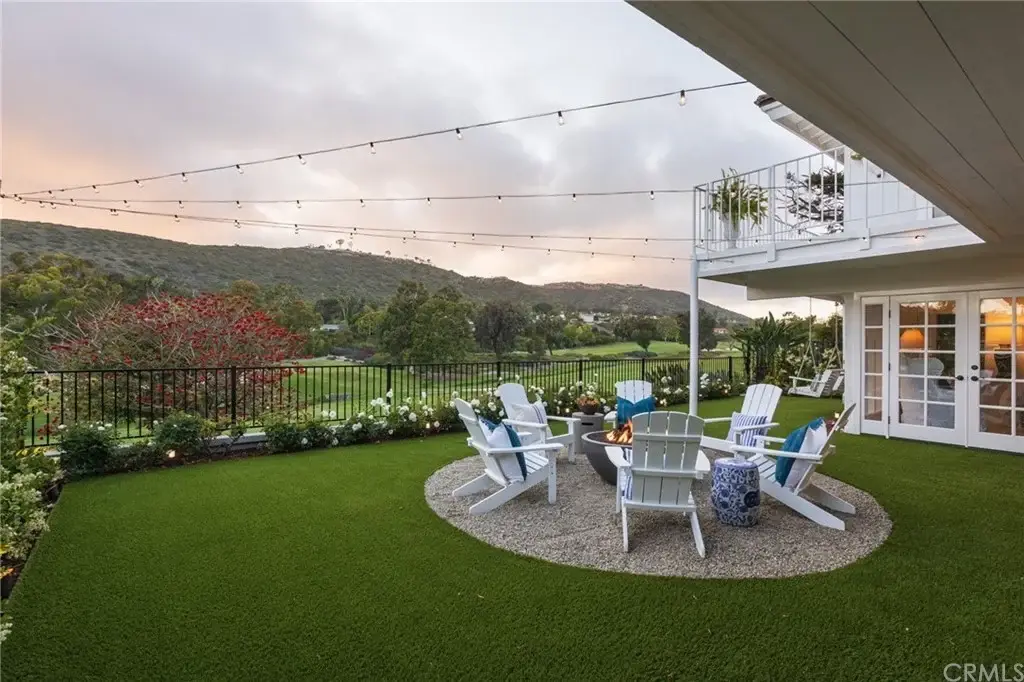 Patio of California real estate house with fire pit, chairs, grass, string lights, and mountain view.