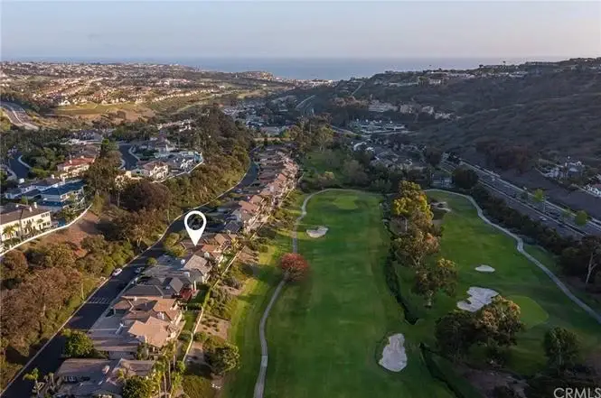 Aerial view of houses California real estate with golf course, hills, ocean, and location marker.