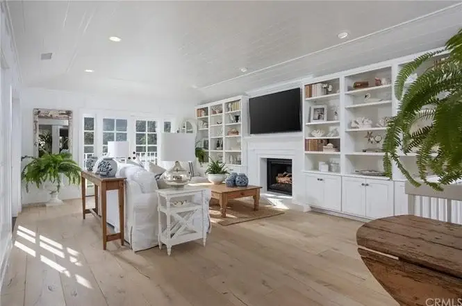 Living room with white sofa, fireplace, wall TV, built in shelves, wood floor, and plants.