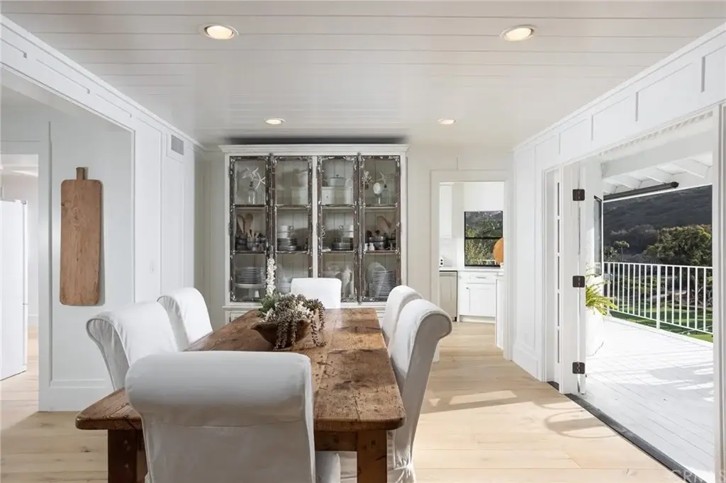Dining area with wood table, white chairs, glass cabinet, and large windows.