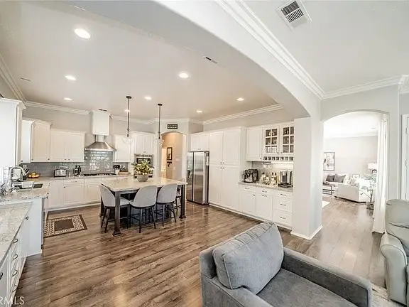 Kitchen with white cabinets, stainless steel appliances, island with seating, and living area in background