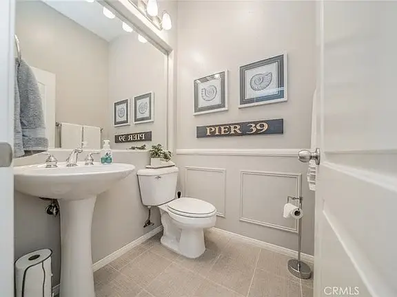 Bathroom with pedestal sink, toilet, light gray walls, framed decorations, and "PIER 39" sign