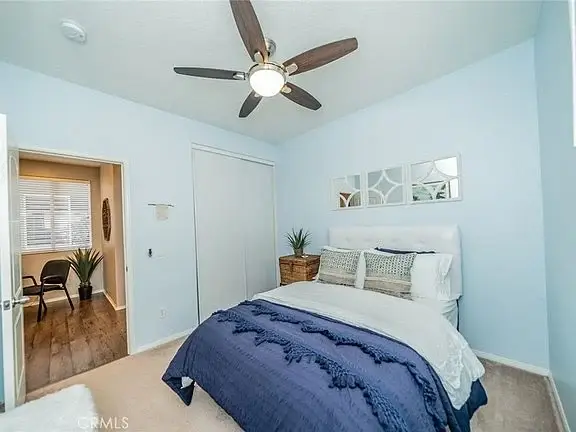 Bedroom with light blue walls, white bed with pillows, ceiling fan, mirror decor, closet, and open door