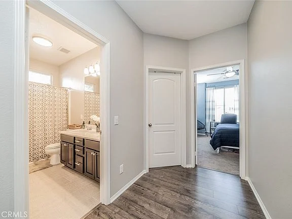Hallway with hardwood floor, light gray walls, doorways to bathroom and bedroom