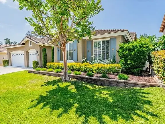 California real estate house with manicured lawn, flower beds, and large tree in front yard