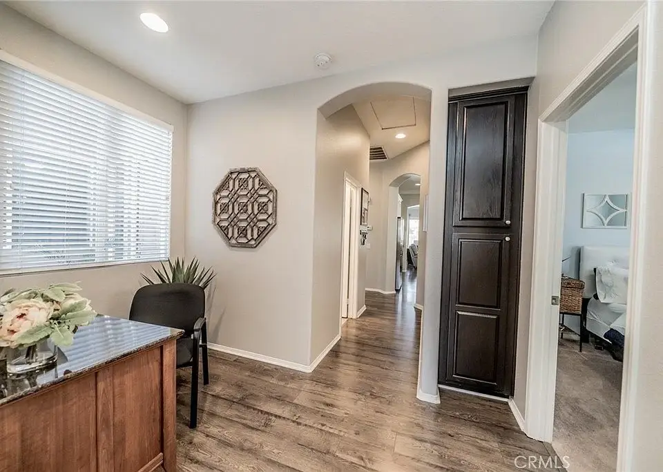 Hallway with wooden floor, small table with flowers, chair, and archway to another room