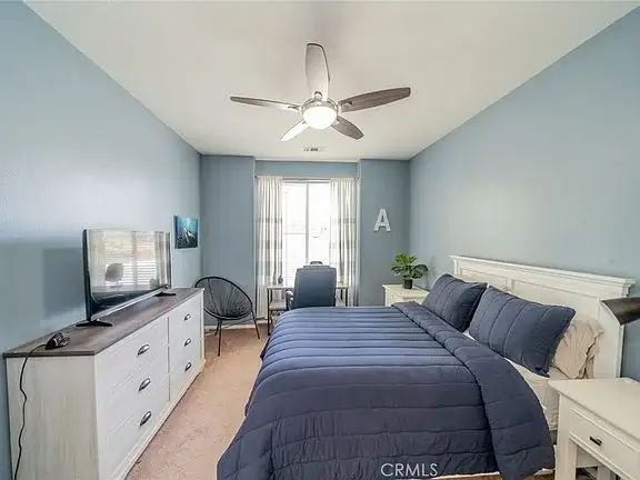 Bedroom with blue accent wall, queen bed with navy bedding, dresser, TV, and armchair near window