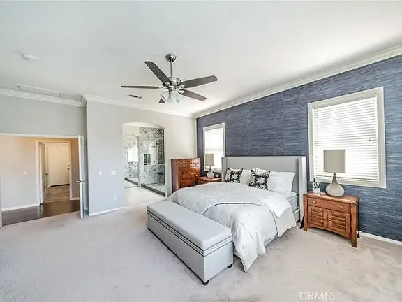 Bedroom with bed, bench, lamps, ceiling fan, blue wall, and bathroom