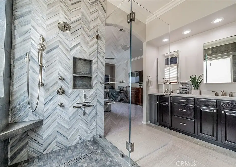 Bathroom with glass shower, herringbone tile, double vanity with dark cabinets, and lighting