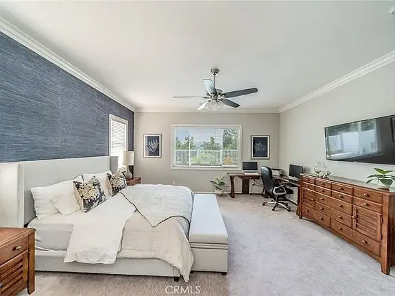 Bedroom with large bed, decorative pillows, ceiling fan, dresser, desk with chair, and framed pictures